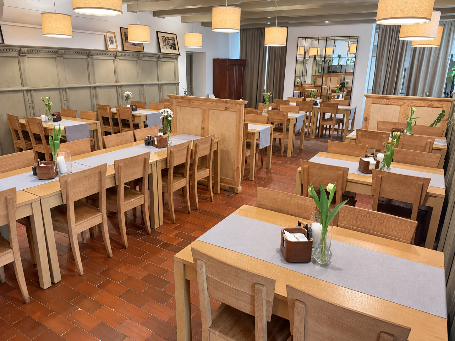 Wnętrze Restauracji Spichlerz — drewniane stoły i krzesła, jasne lampy oraz kwiaty